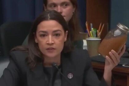 Alexandria Ocasio-Cortez sostiene un bote de agua marrón junto a centro de datos de Meta
