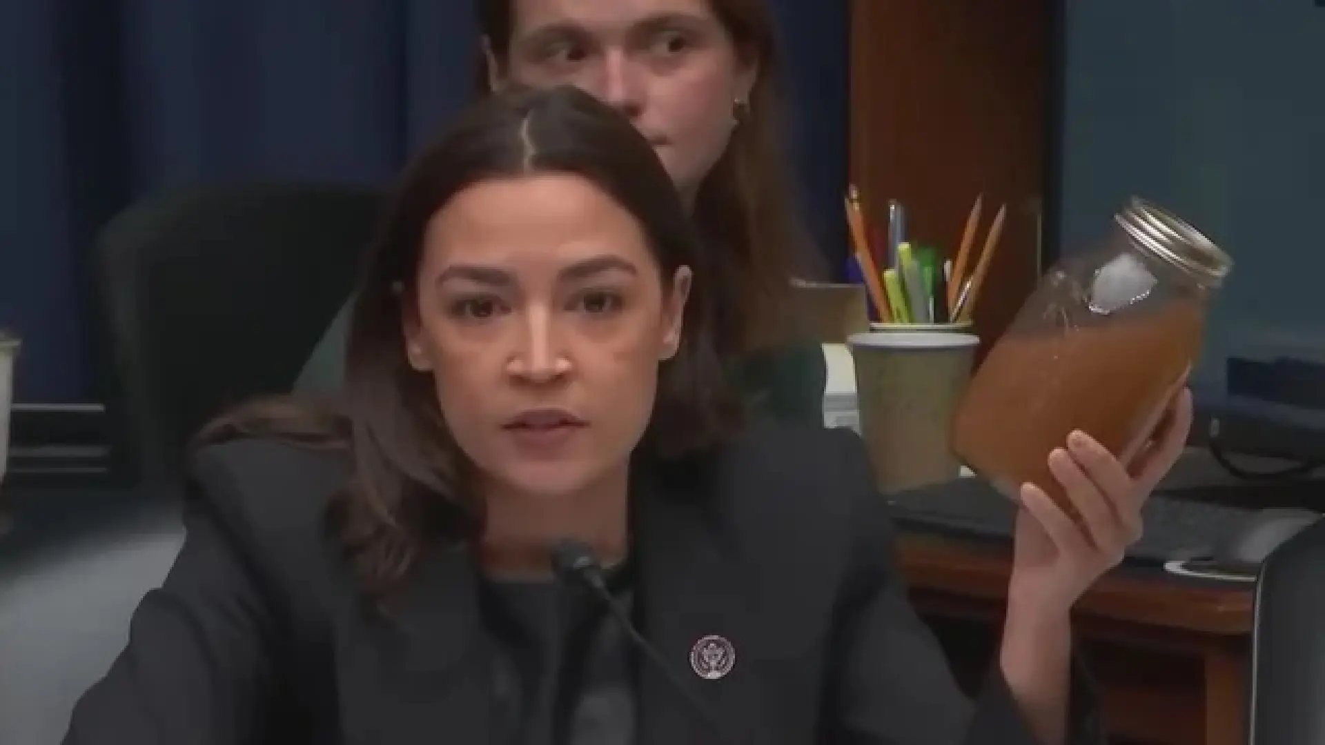 Alexandria Ocasio-Cortez sostiene un bote de agua marrón junto a centro de datos de Meta