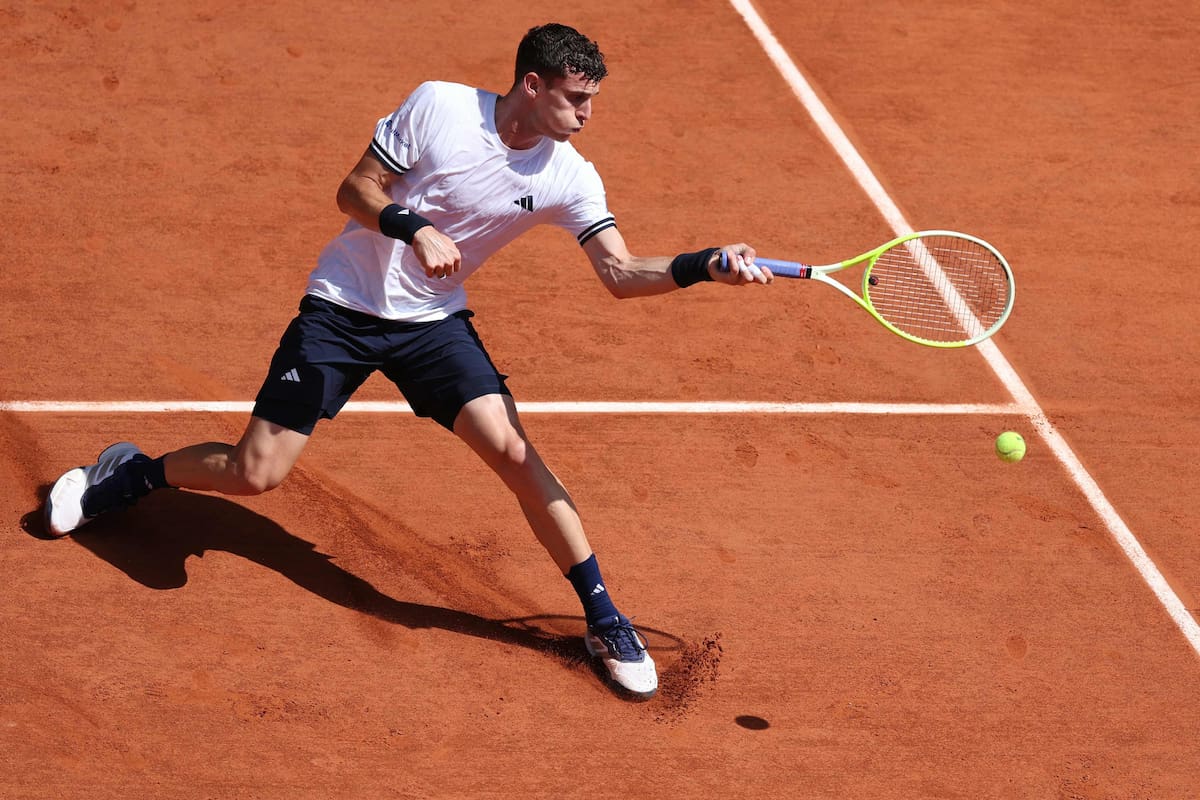 Juan Manuel Cerúndolo en acción durante un partido de Roland Garros, con una expresión de concentración y esfuerzo.